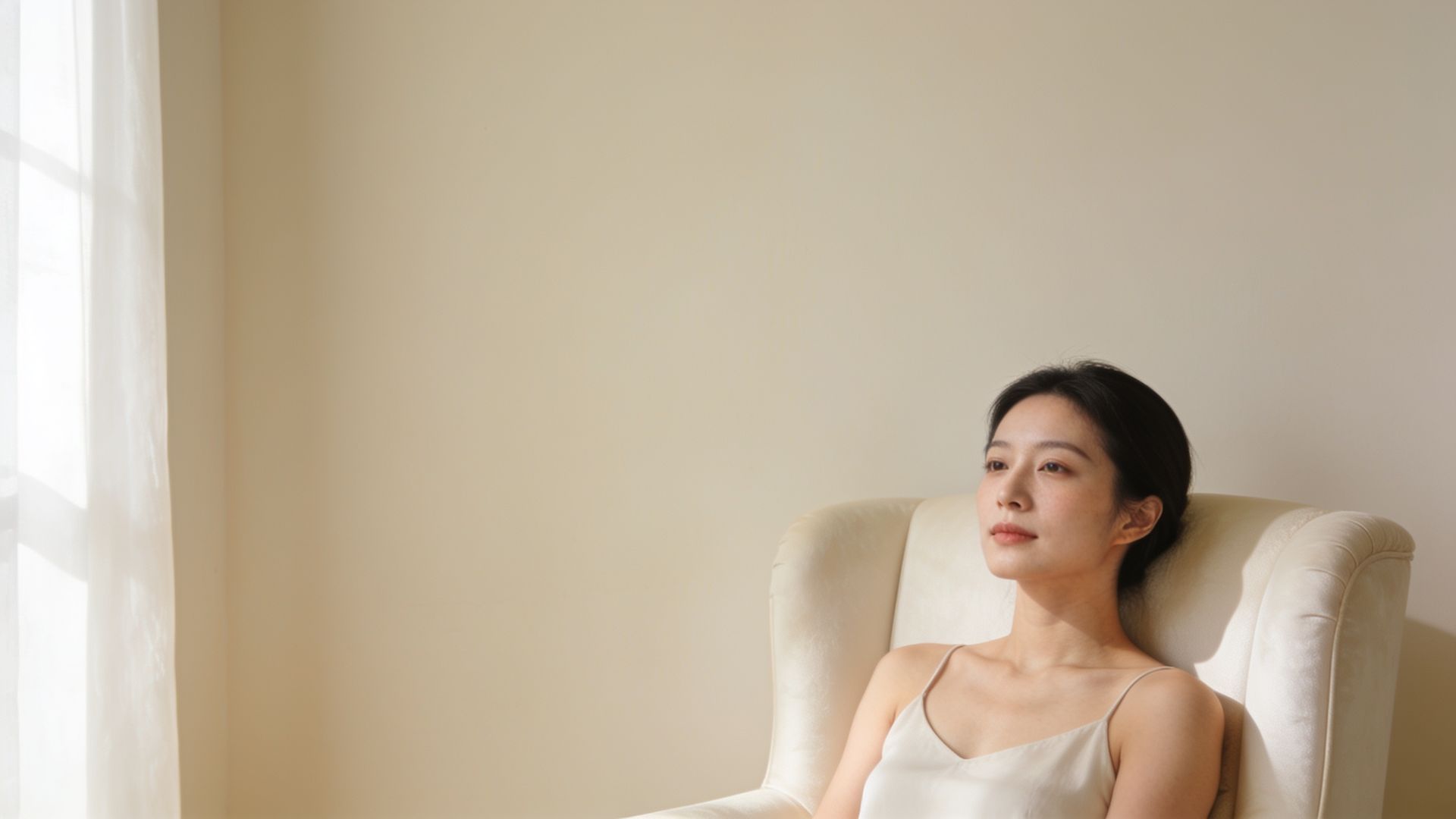 Relaxed East Asian woman with clear skin seated in soft window light