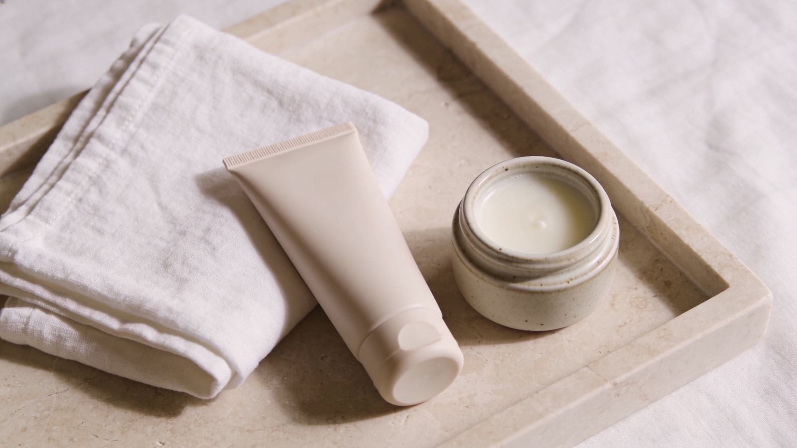 Plain sunscreen, a bland balm and a folded towel on stone, representing simple post-laser care in hot weather