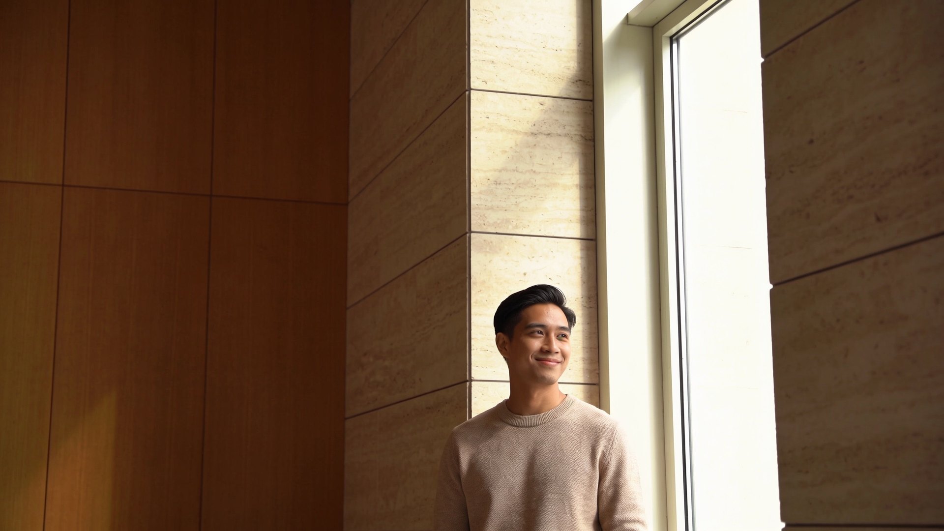 A Southeast Asian man in his late twenties with natural skin, standing by a sunlit window, representing boxcar scar treatment at IN Eternity Clinic, Singapore
