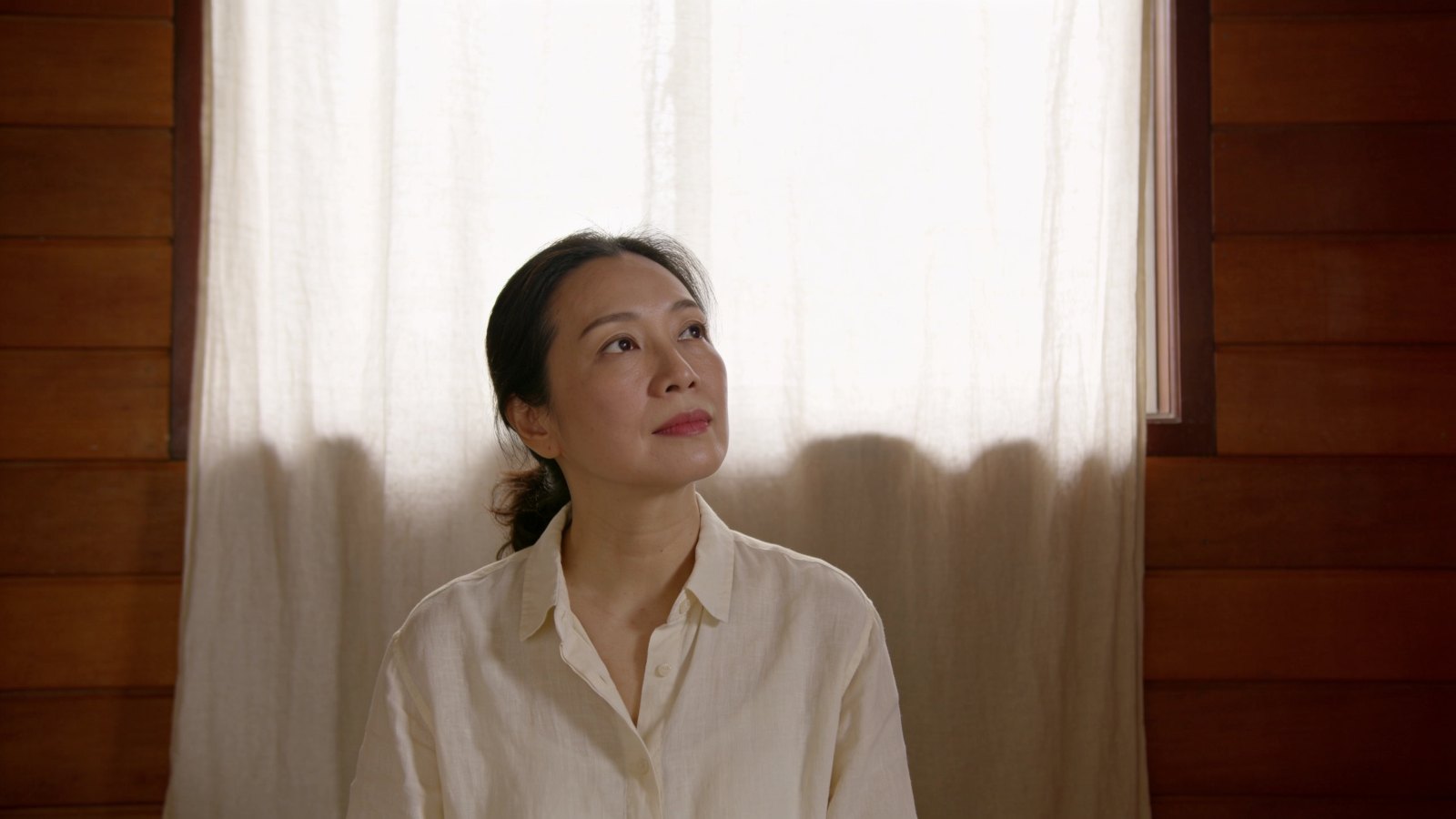 A woman in her early forties looking calmly towards soft window light, her whole head and face in frame with relaxed eyes