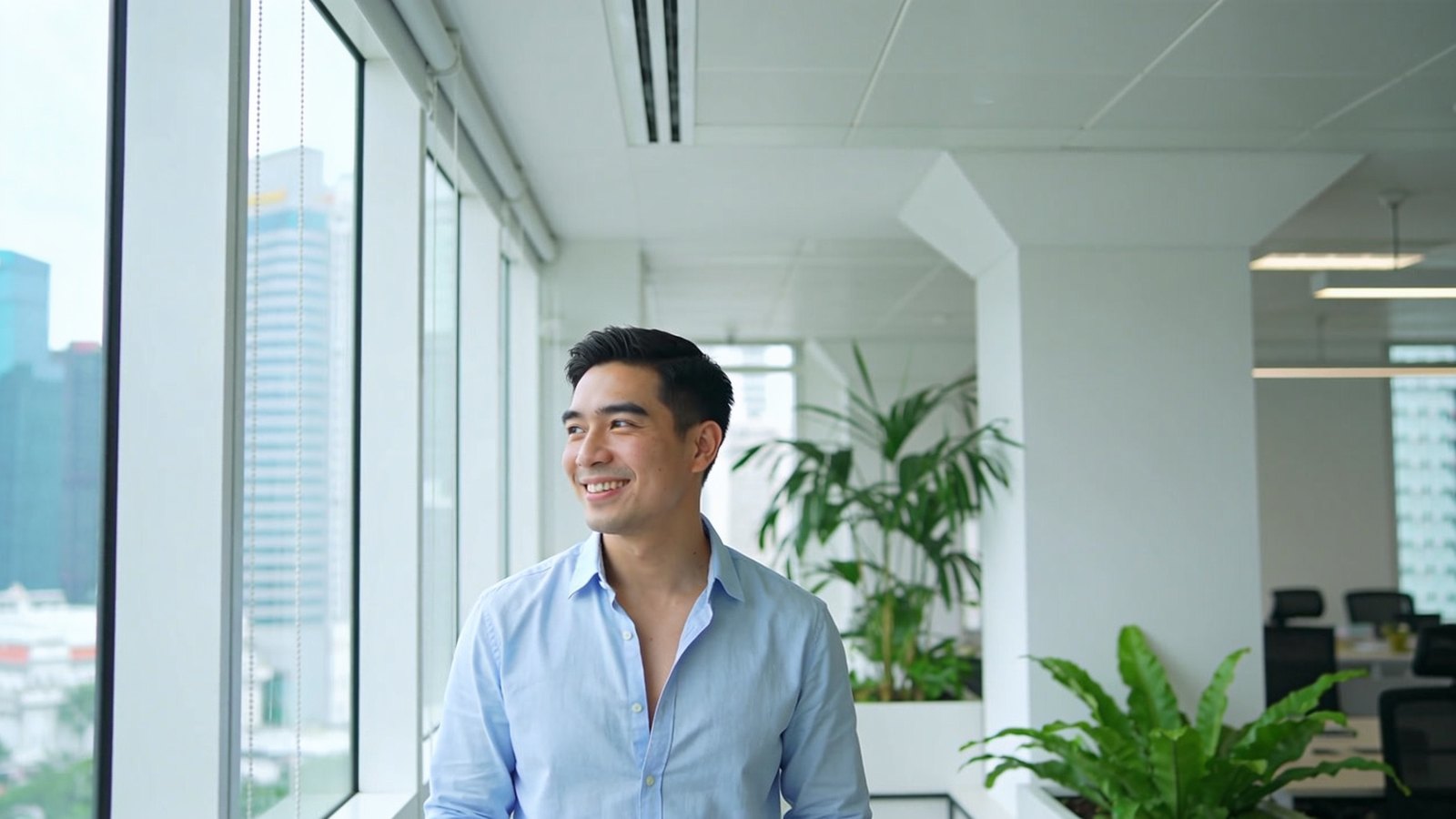 East Asian man in his mid-thirties with full, natural-looking brows, smiling in a bright office with his whole head and face in frame
