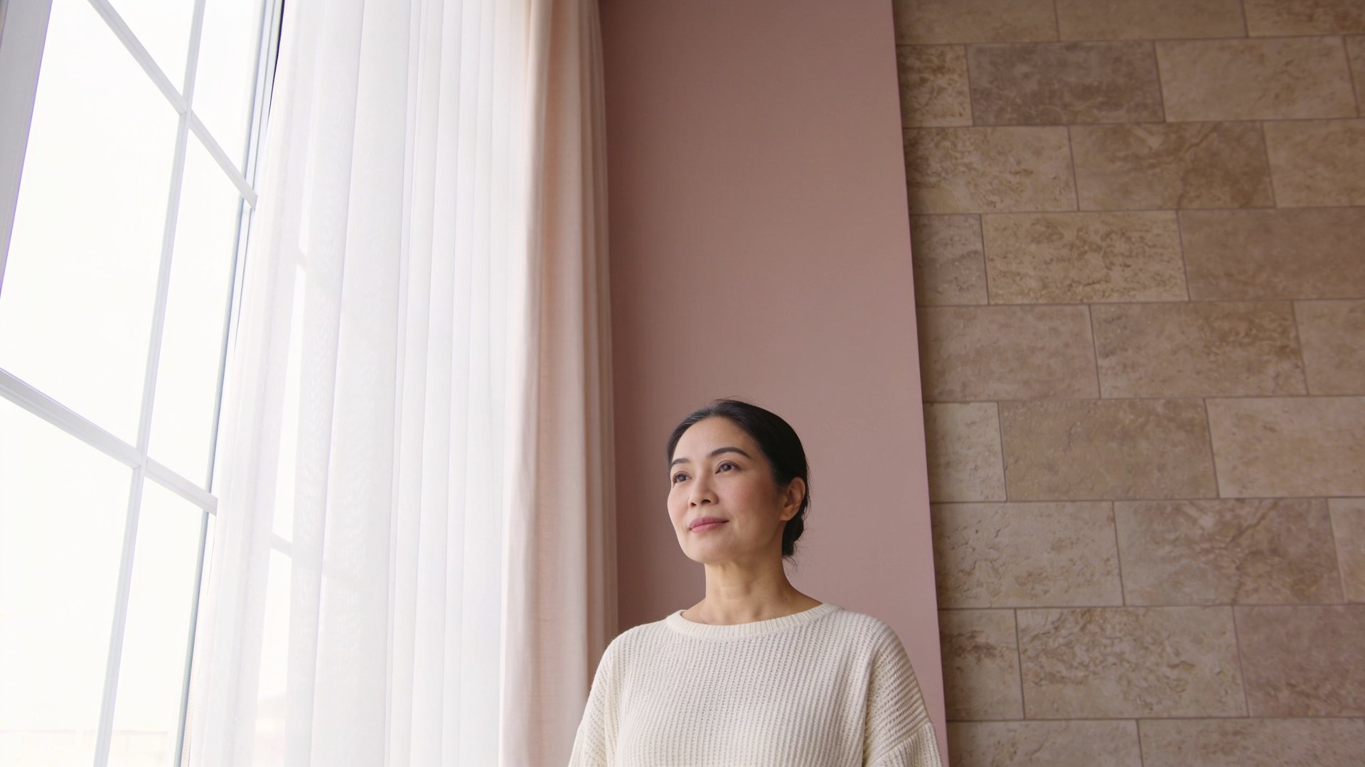 Southeast Asian woman in her forties with relaxed, open eyes standing by a bright window, representing hooded eyes treatment at IN Eternity Clinic, Singapore
