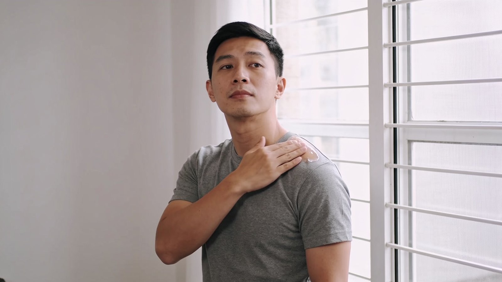 A man applying a clear silicone scar gel near his collarbone at home in daylight