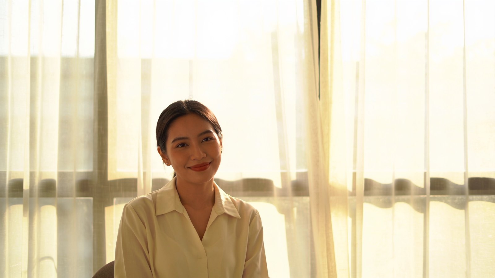 Southeast Asian woman in her late twenties with naturally rosy lips, smiling softly in daylight, her whole head and face in frame