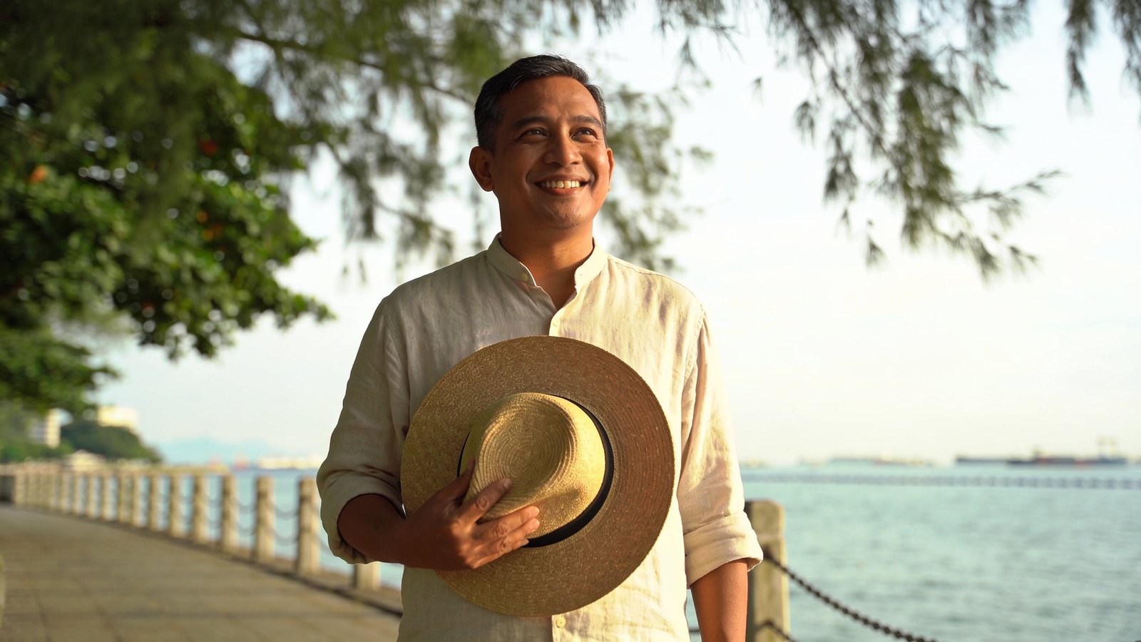 A Malay Singaporean man in his forties smiling in soft outdoor shade, his whole head and face in frame