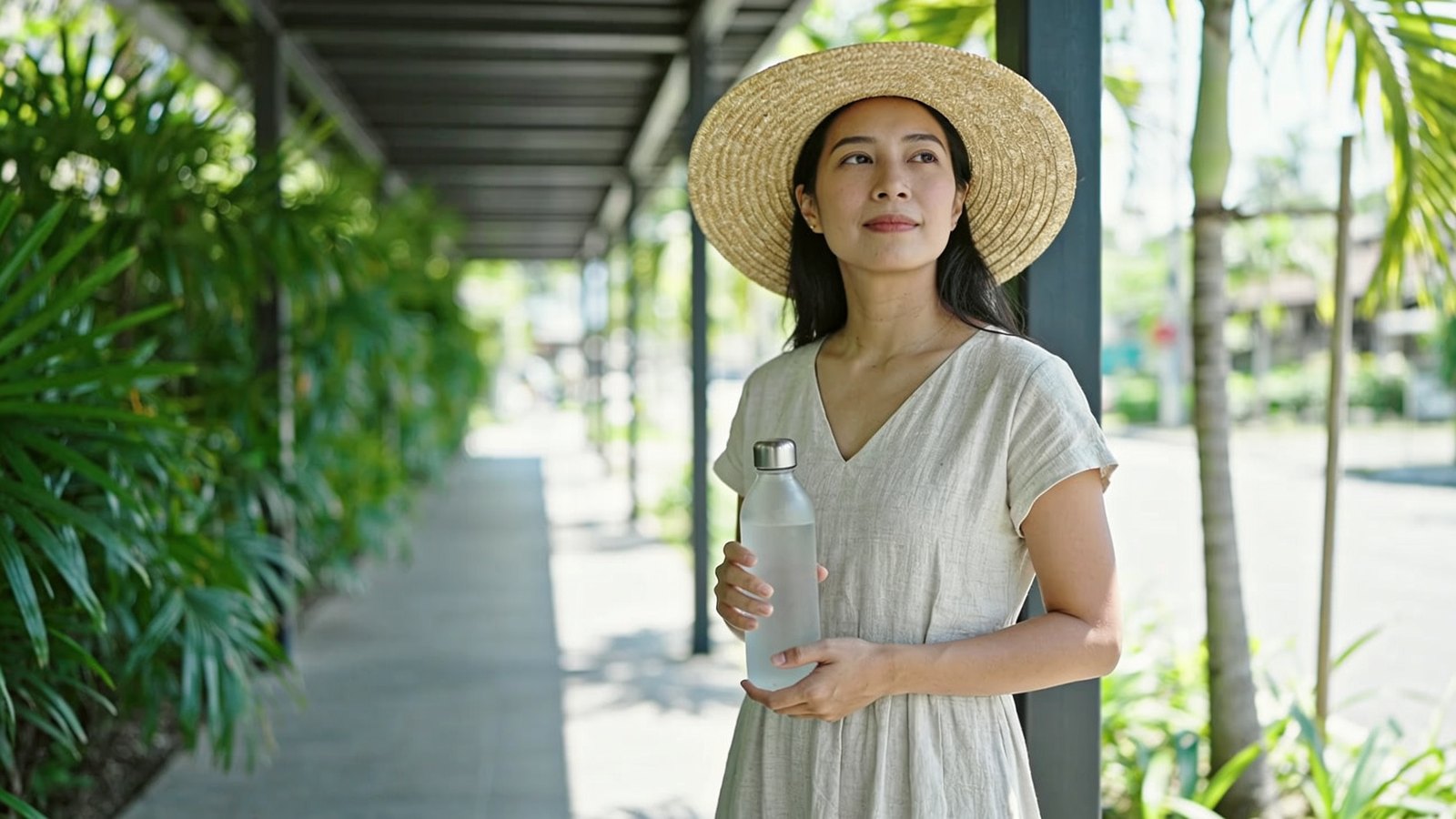 A Southeast Asian woman in her thirties resting in the shade of a covered walkway on a hot Singapore afternoon, her whole head and face in frame