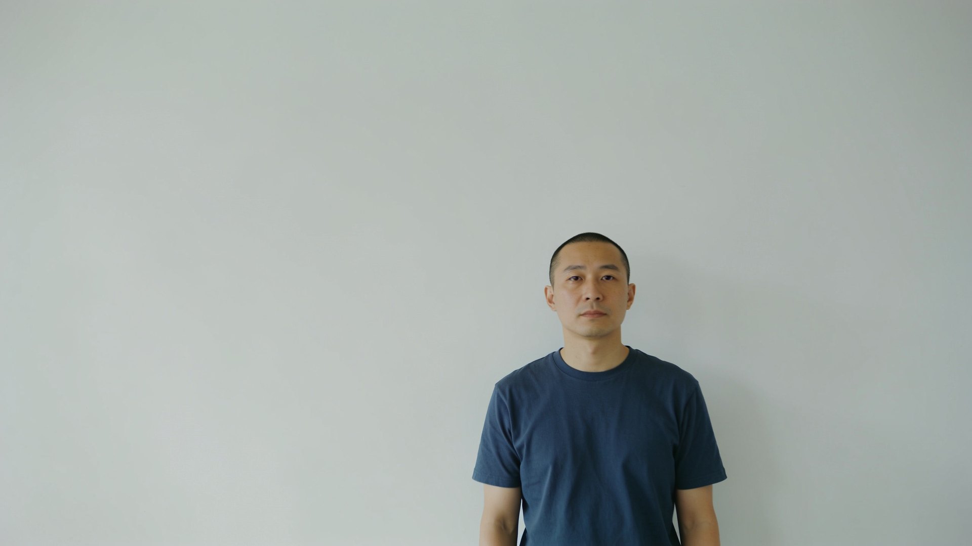 East Asian man in his late thirties with a neat buzz-cut look, photographed waist-up against a plain wall, representing scalp micropigmentation at IN Eternity Clinic, Singapore