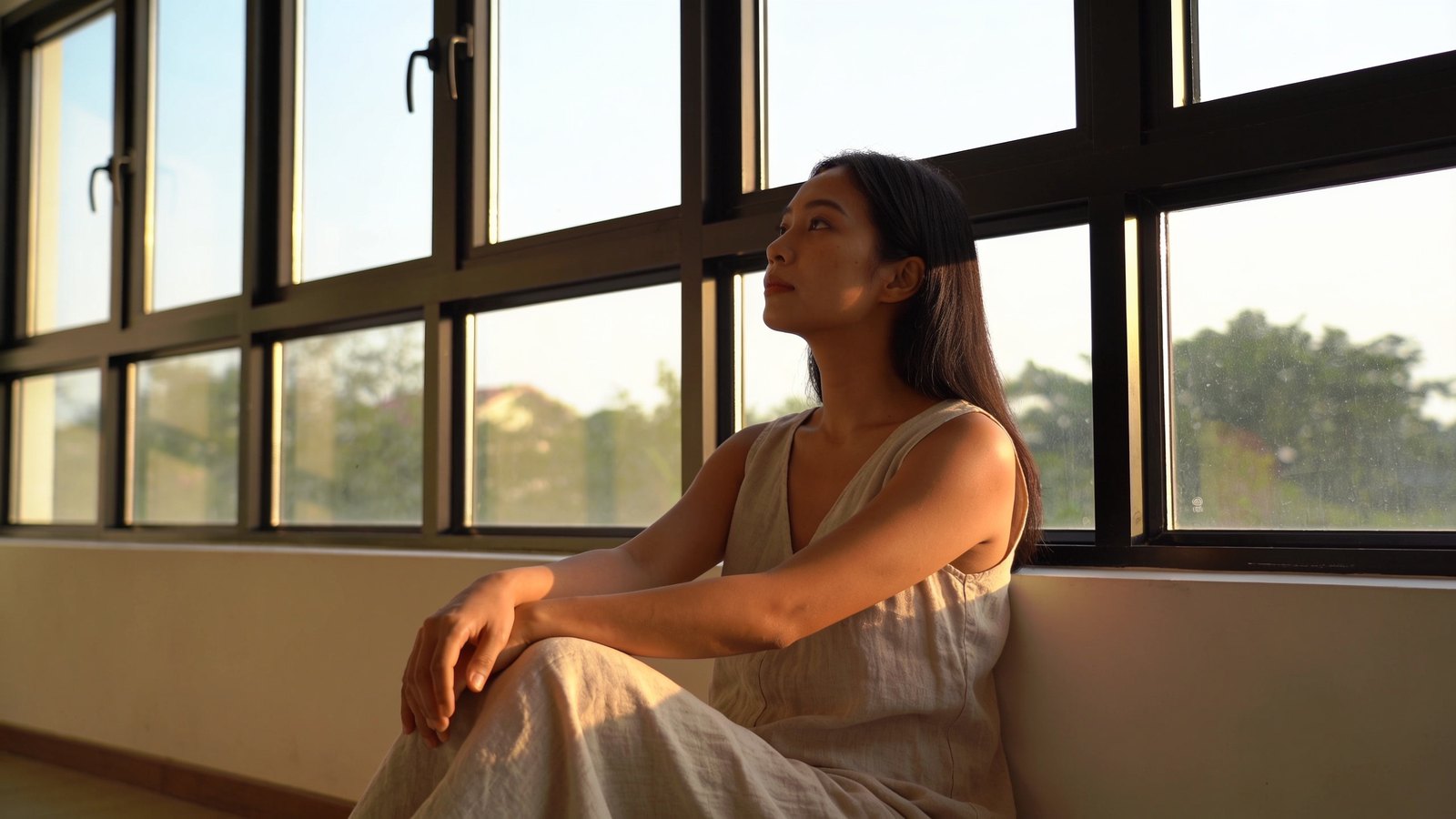 A woman with clear, even skin in warm daylight, looking calmly towards the window
