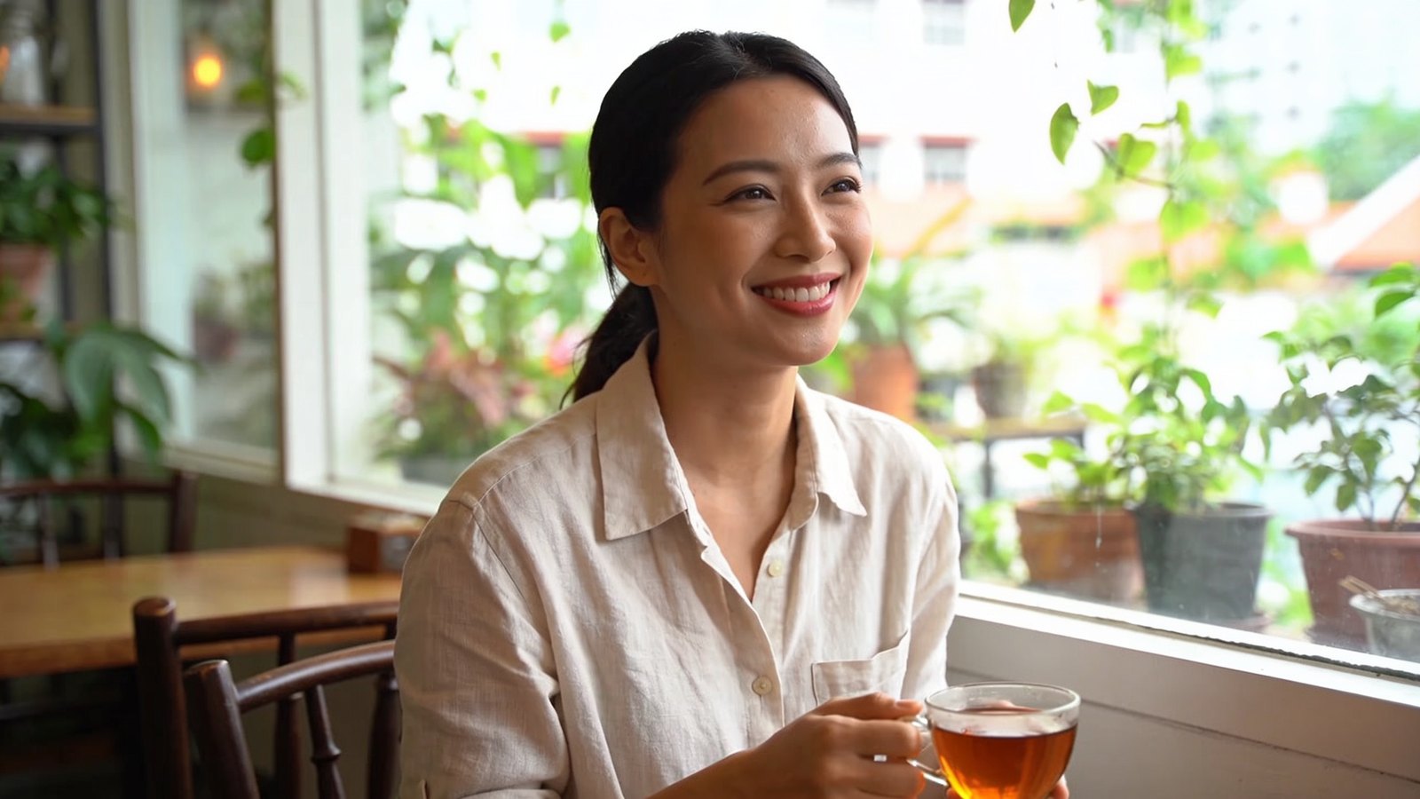 A Chinese Singaporean woman in her thirties smiling in a bright café by the window, her whole head and face in frame